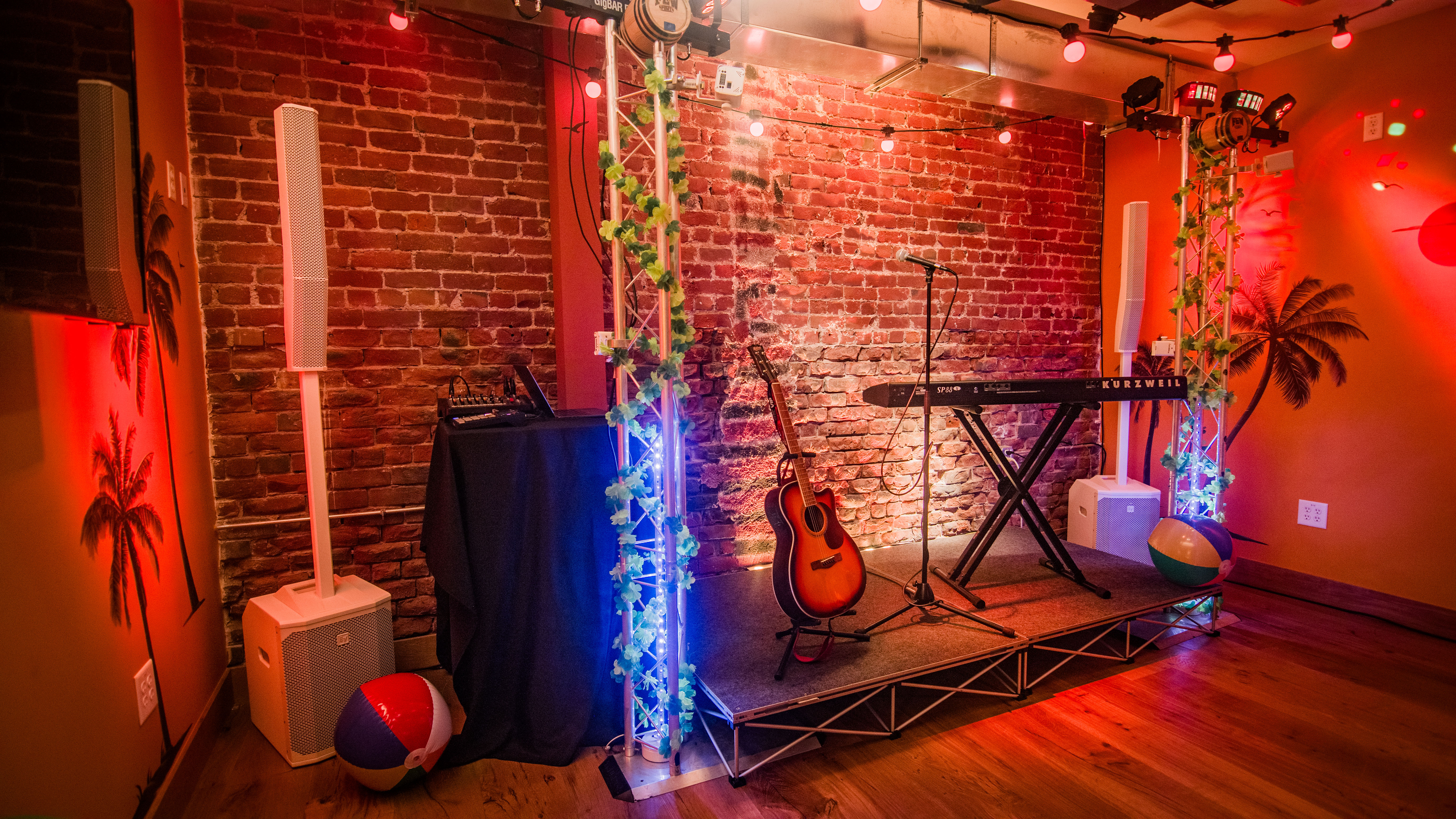 A stage with a guitar, keyboard, and speaker in a room with a brick wall and red lighting.
