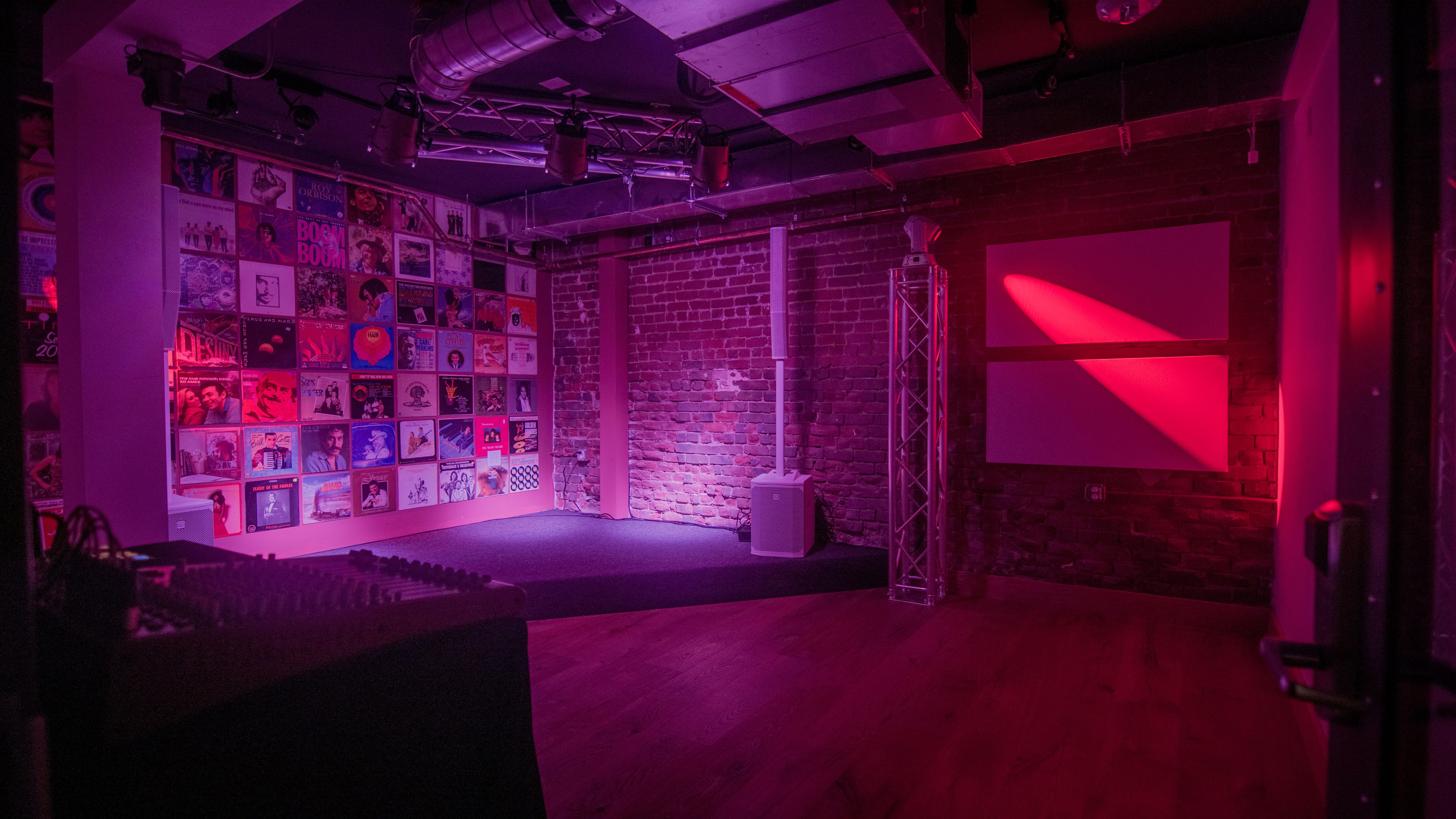 A dimly lit room with a stage, brick walls covered in vinyl records, and red lighting.