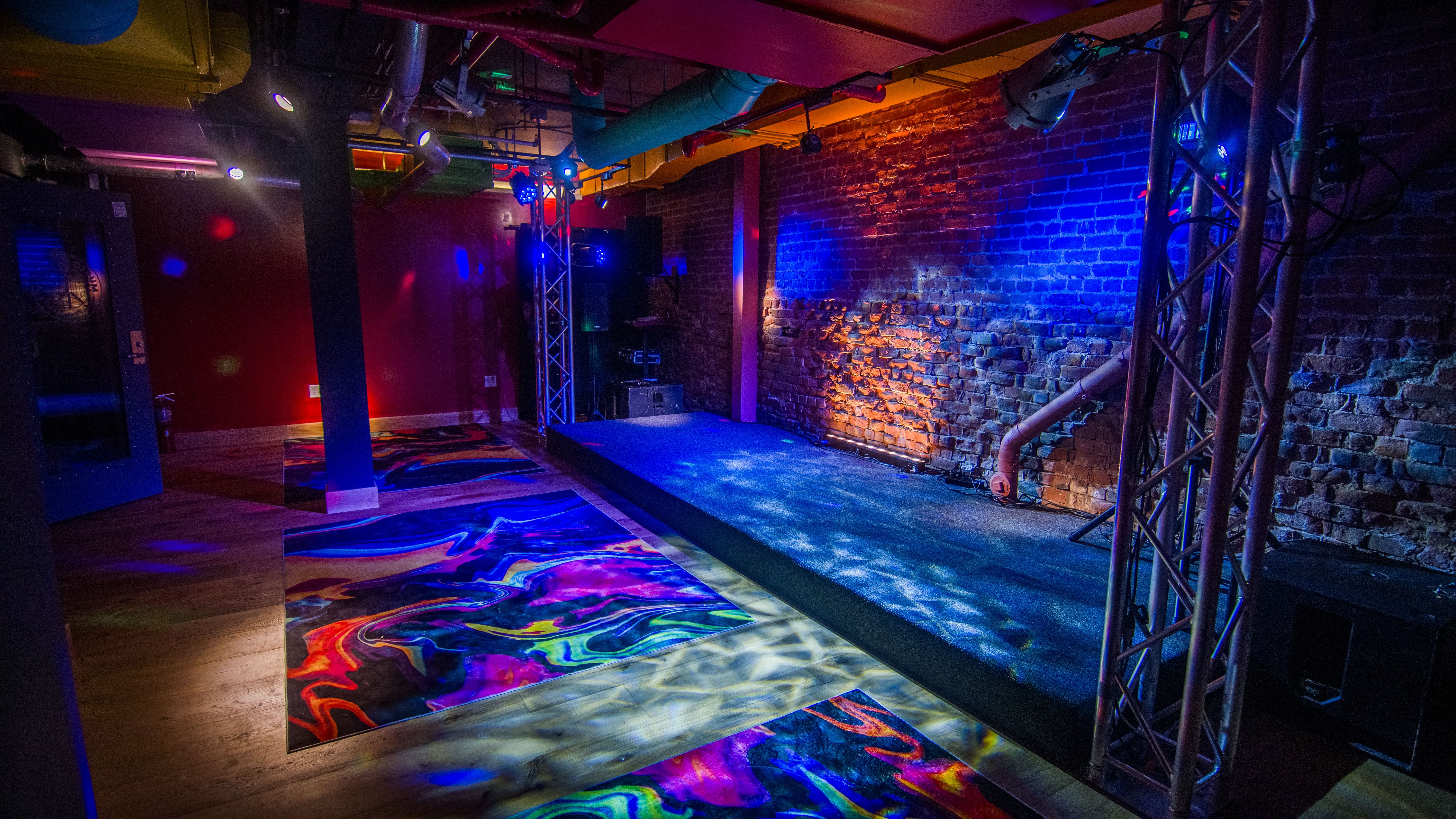 A dimly lit room with a stage, brick walls, and colorful lighting.