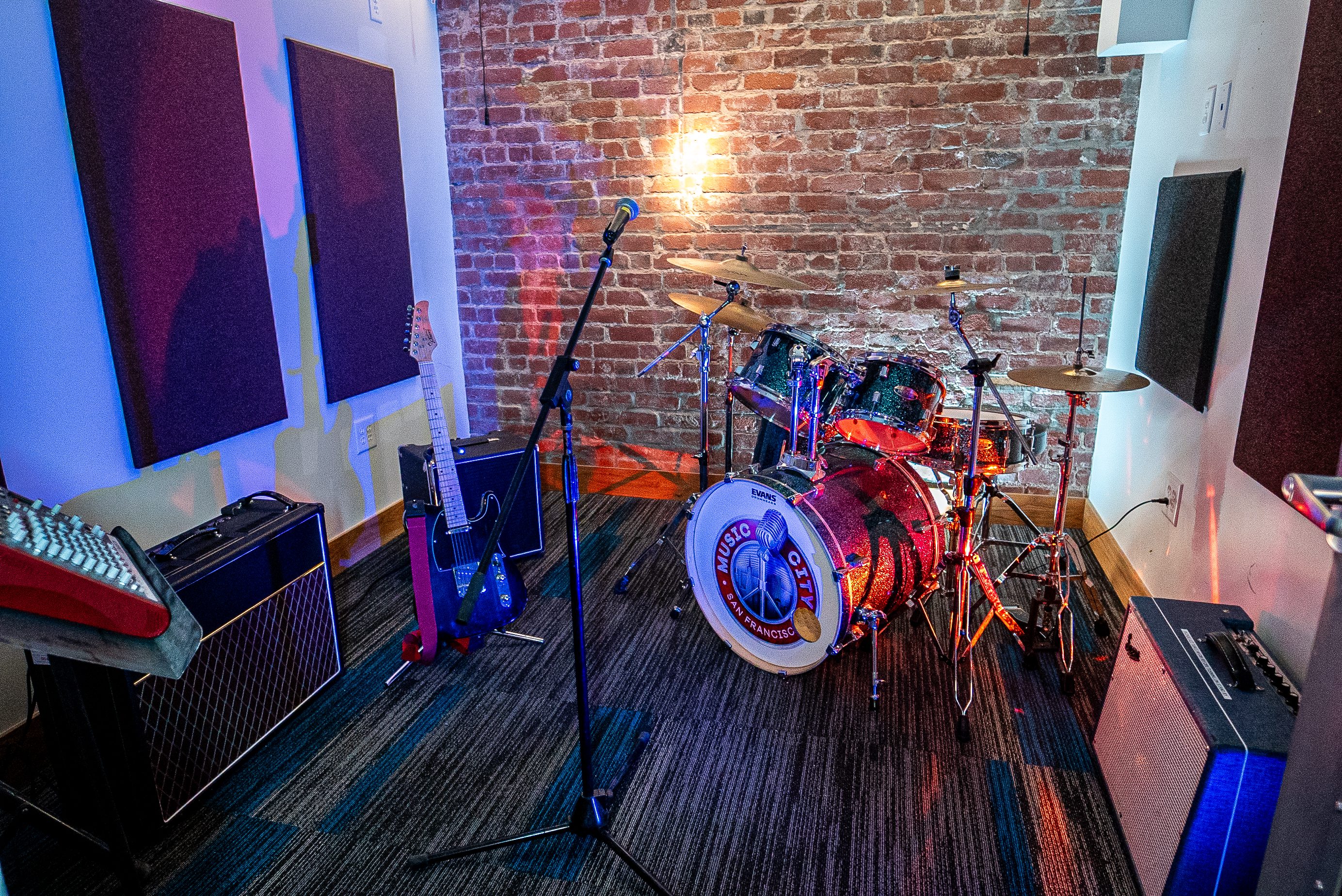 A music room with a drum set, guitar, amplifiers, and microphone in front of a brick wall.