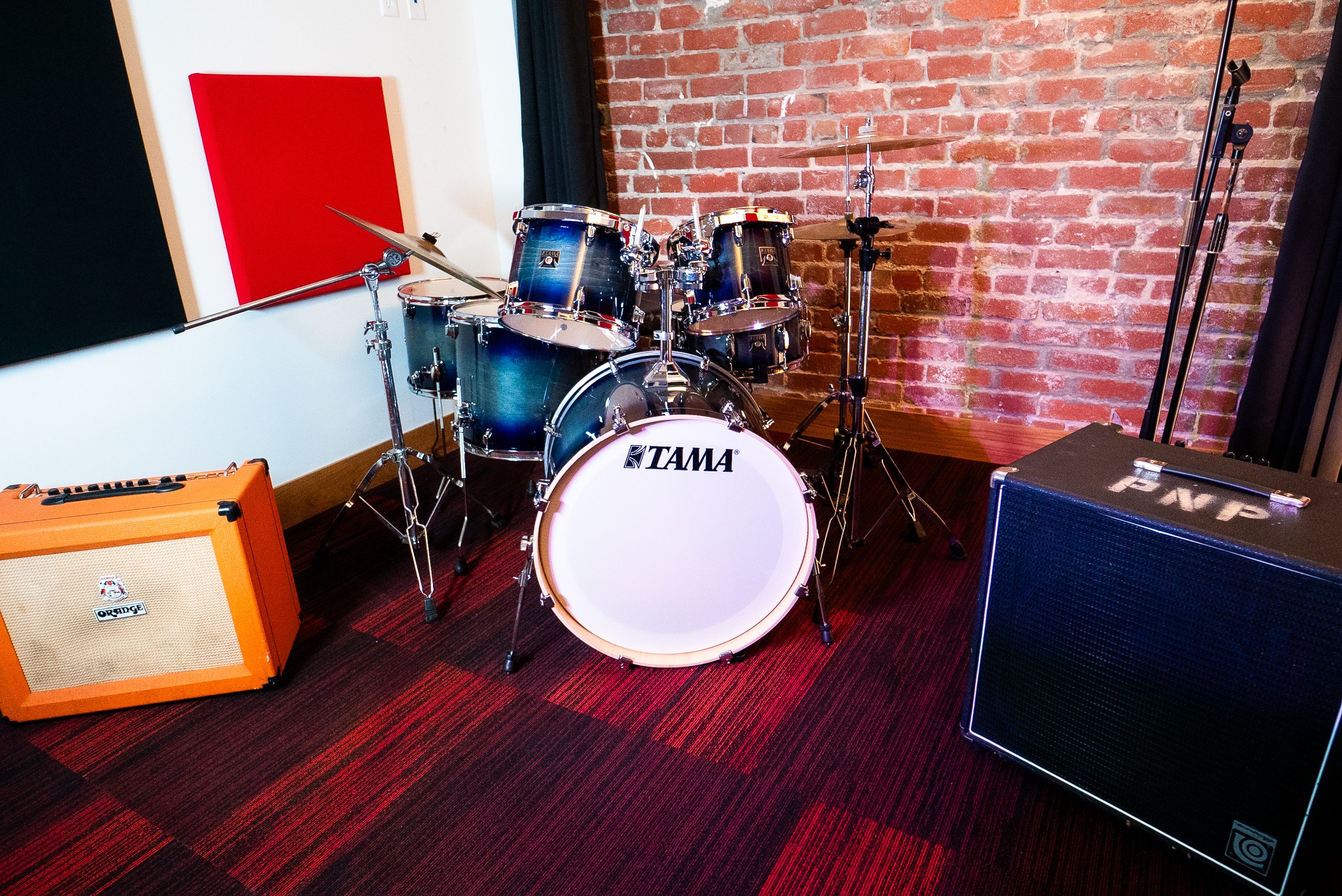 A drum set and musical equipment in a room with a brick wall and acoustic panels